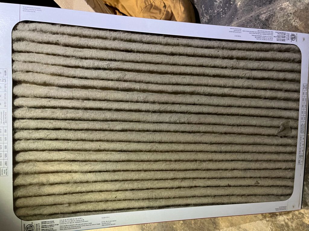 A close up look at the grooves in an HVAC filter that are clogged with dust, dirt, hair, and other debris.